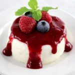 Keto Panna Cotta on white round plate with raspberry sauce and fresh berries on top