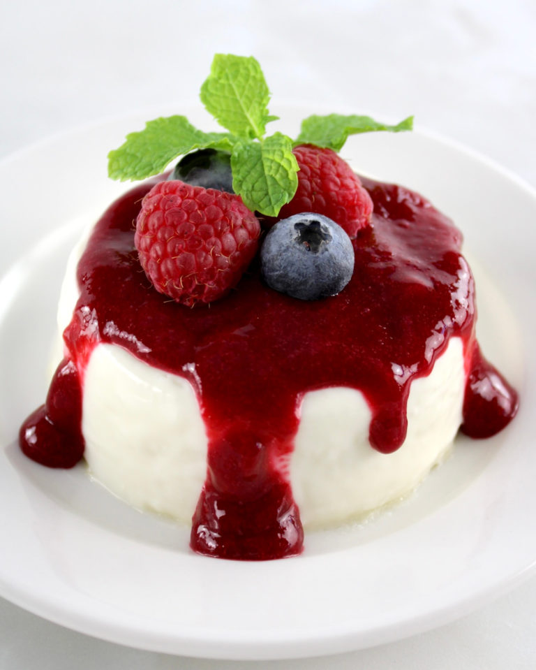 Keto Panna Cotta on white round plate with raspberry sauce and fresh berries on top