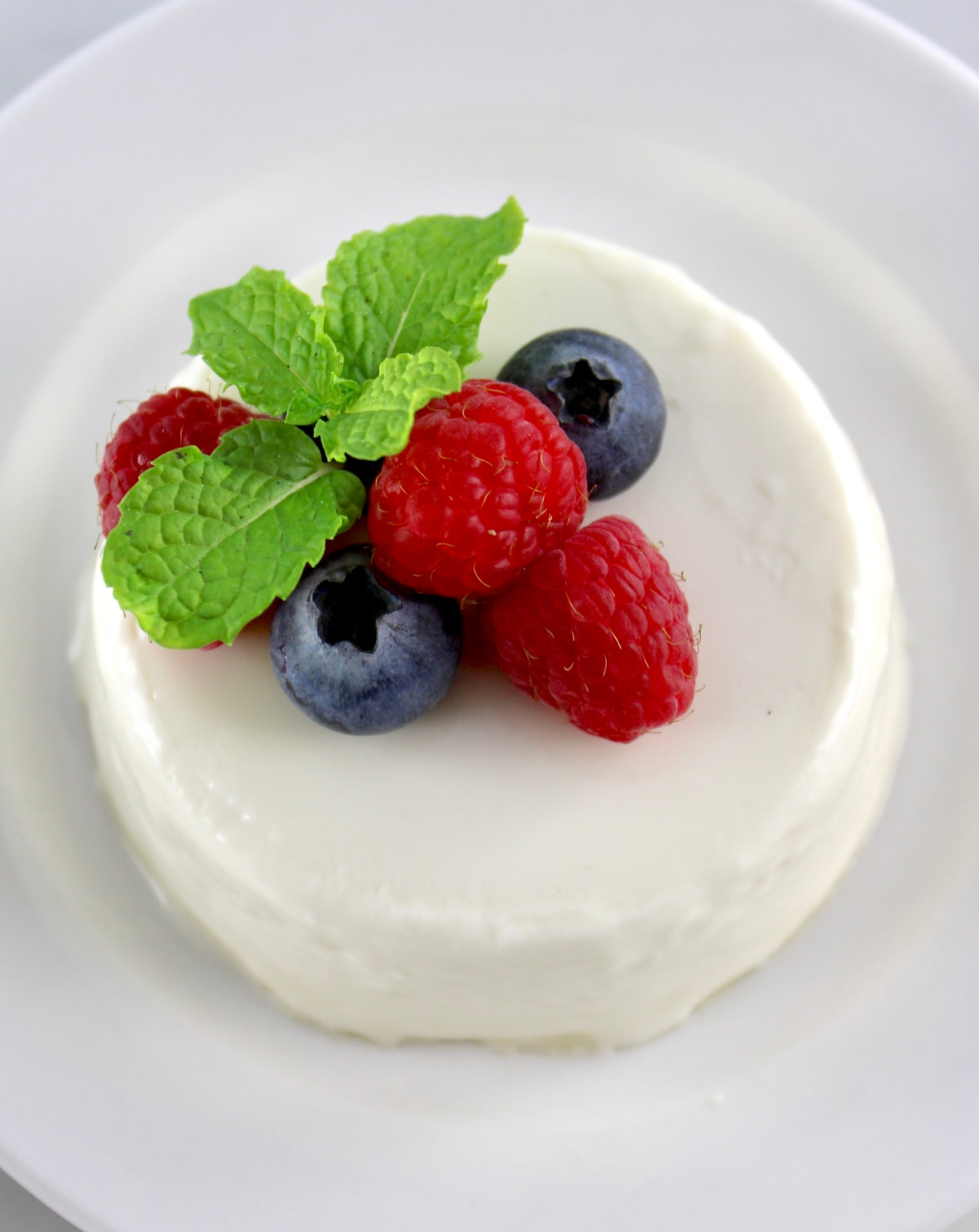 Keto Panna Cotta on white round plate with berries and mint on top