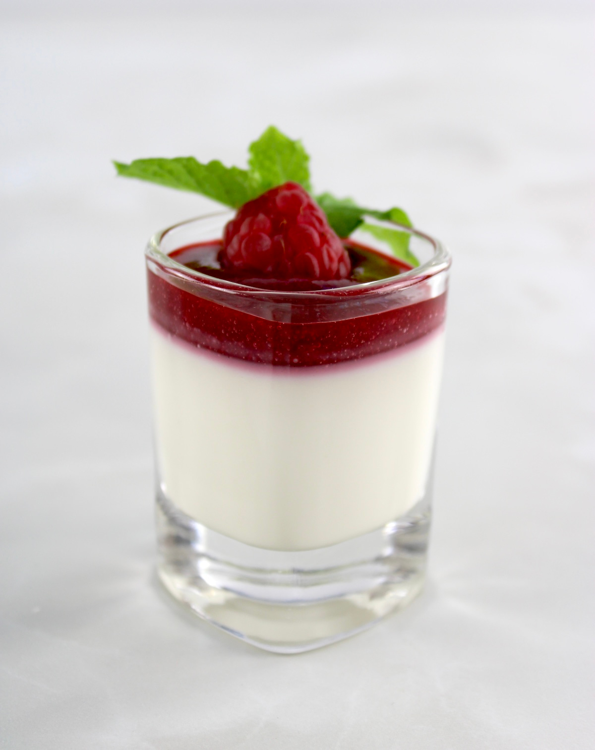 Keto Panna Cotta in shot glass with raspberry, sauce, fresh raspberry and mint on top