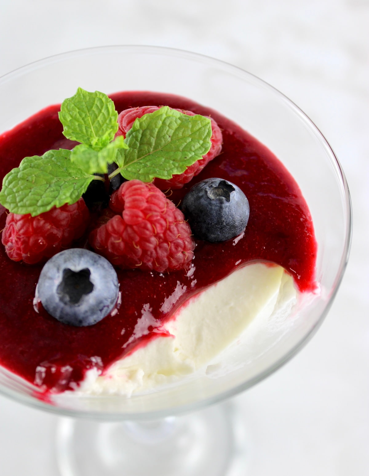 Keto Panna Cotta in martini glass with raspberry sauce and berries with bite missing