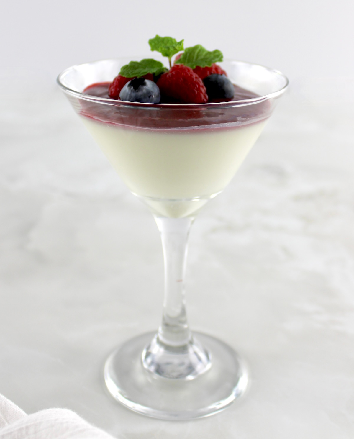 Keto Panna Cotta in martini glass with berries and raspberry sauce on top
