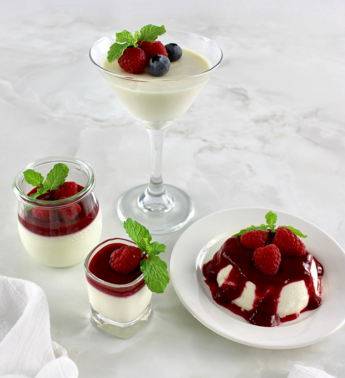 Keto Panna Cotta served in various glasses with raspberry sauce and berries on top