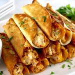 Mini Chicken Taquitos stacked up on white plate with chopped cilantro