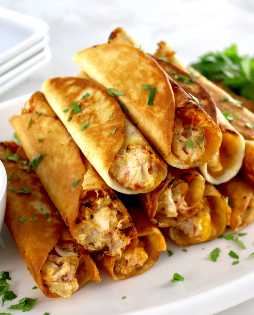 Mini Chicken Taquitos stacked up on white plate with chopped cilantro