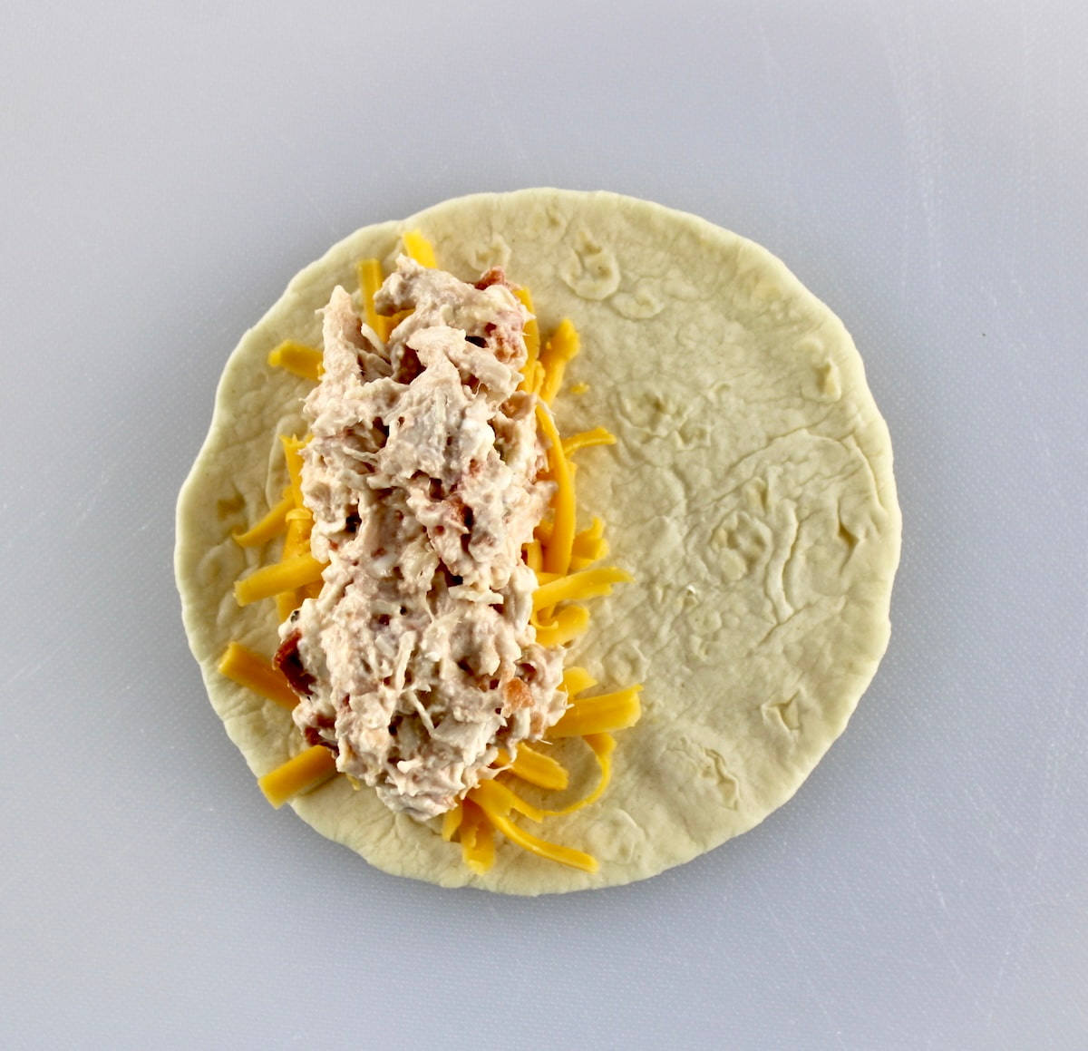 tortilla with shredded cheese and chicken filling on half
