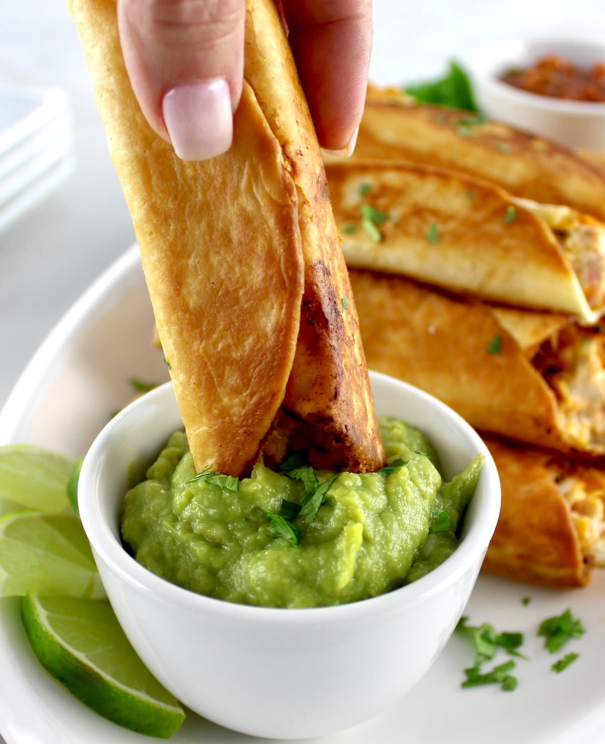 dipping Mini Chicken Taquito into guacamole in white cup
