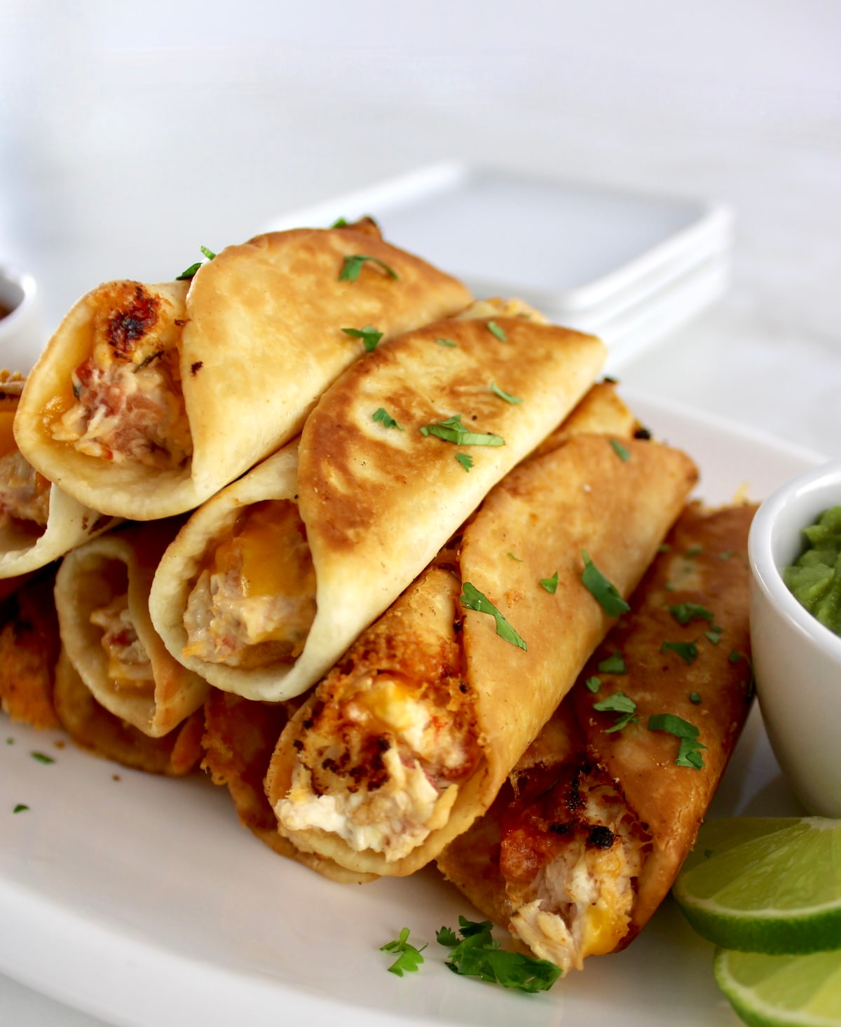 closeup of Mini Chicken Taquitos stacked up on white plate