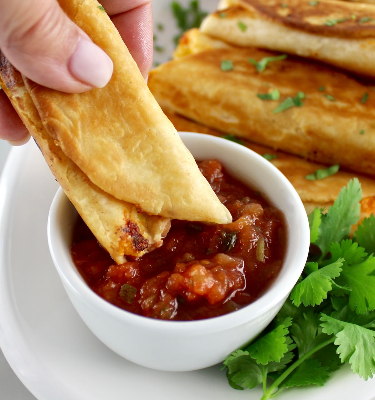 dipping Mini Chicken Taquito in salsa in white cup