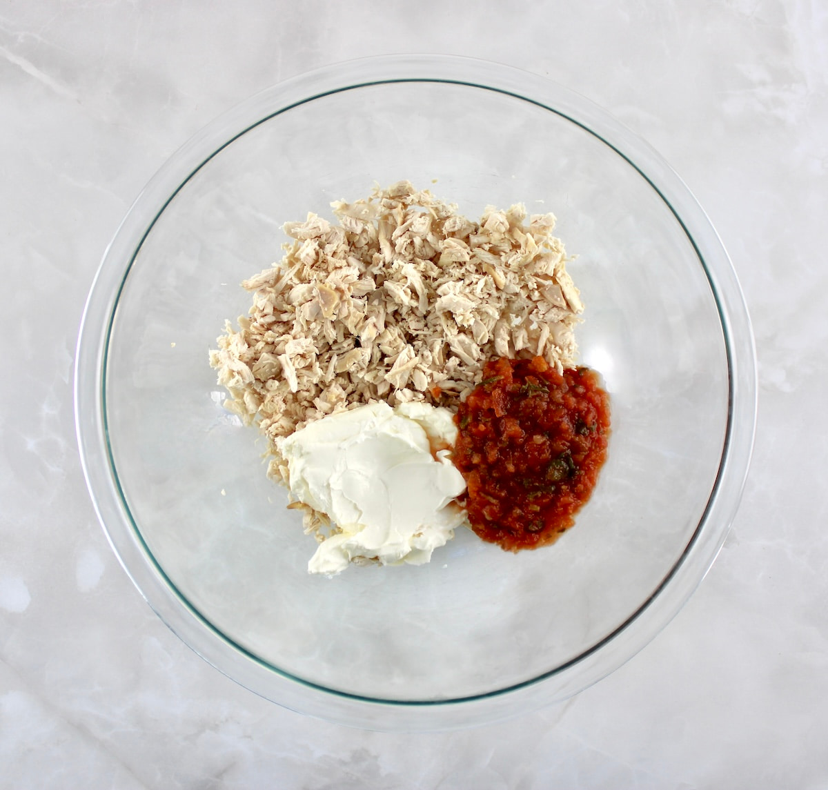 chopped cooked chicken, salsa and cream cheese in glass bowl in sections