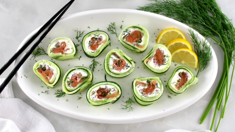 overhead view of Salmon Cucumber Rolls on white oval plate with lemon slices and chopsticks on side