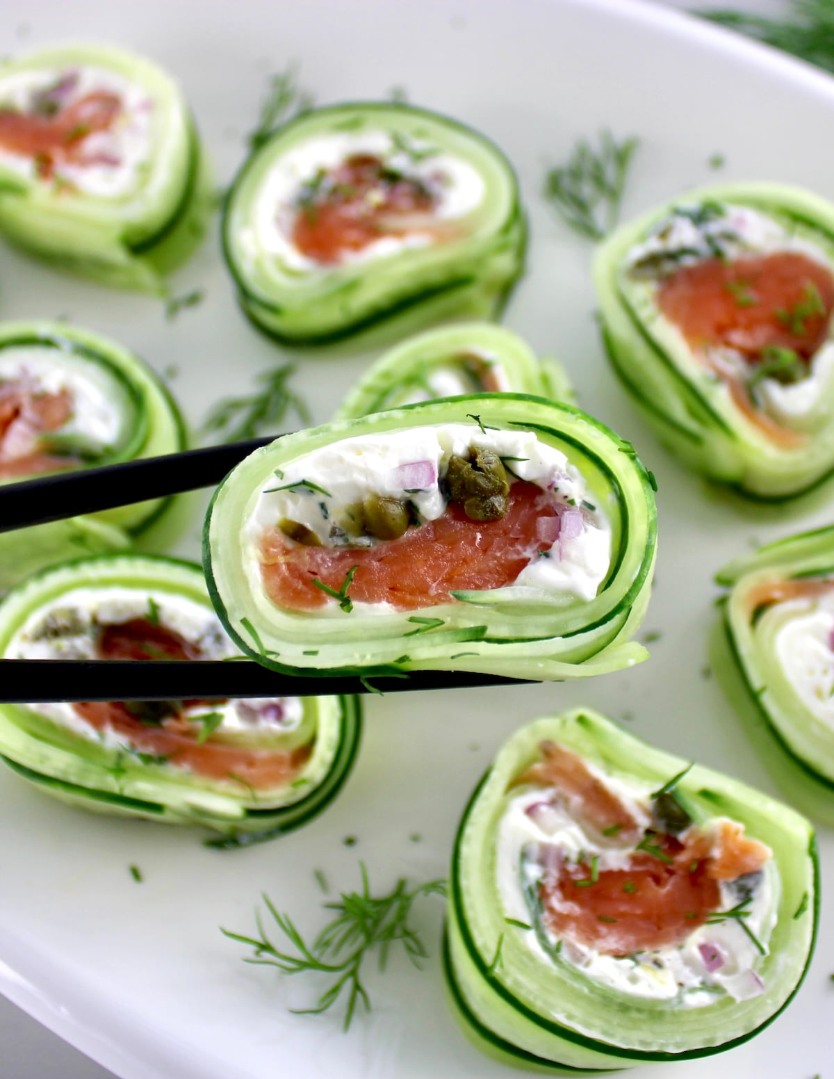 holding up Salmon Cucumber Roll with black chopsticks