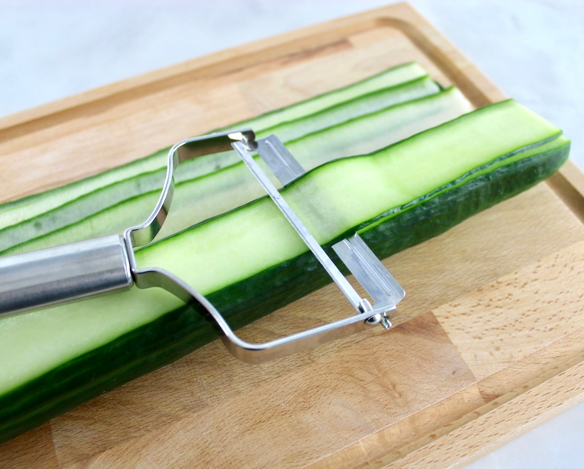 thinly sliced cucumber with peeler on cutting board