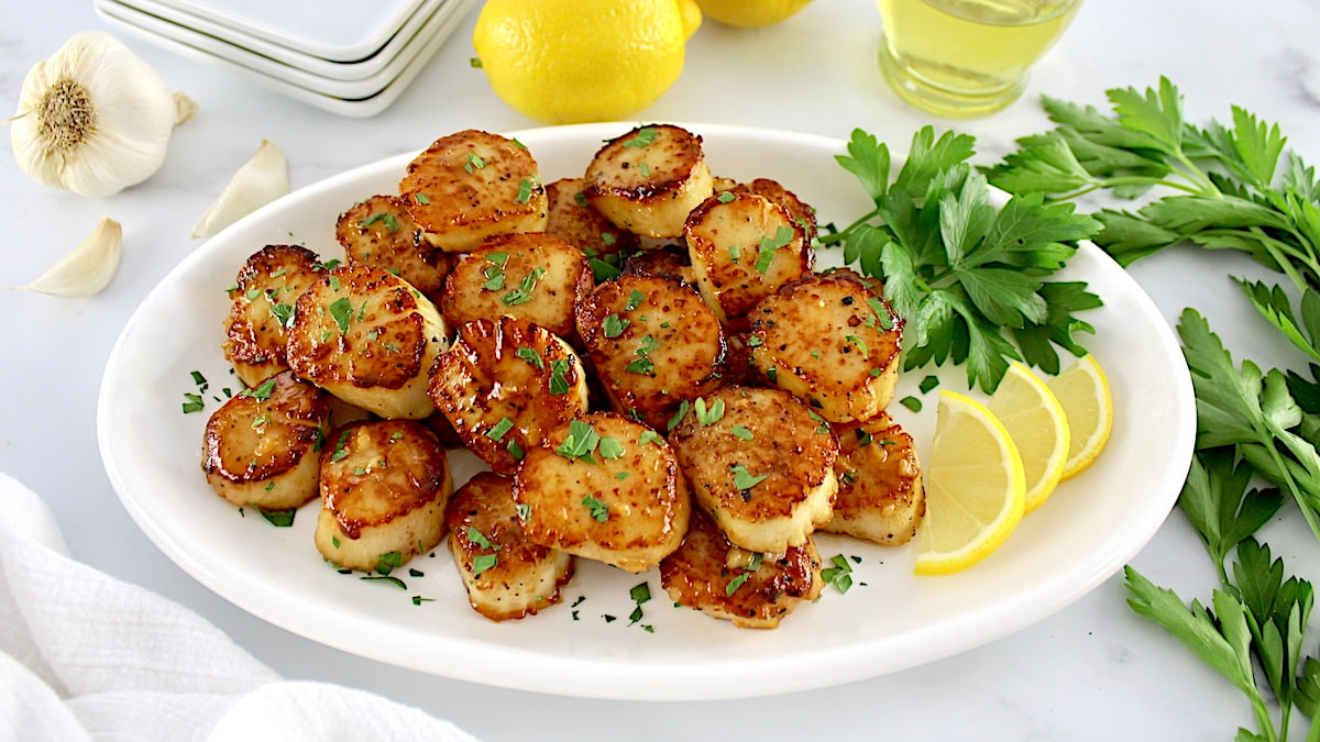 Seared Scallops with Garlic Butter in white oval platter with lemon slices and fresh parsley on side