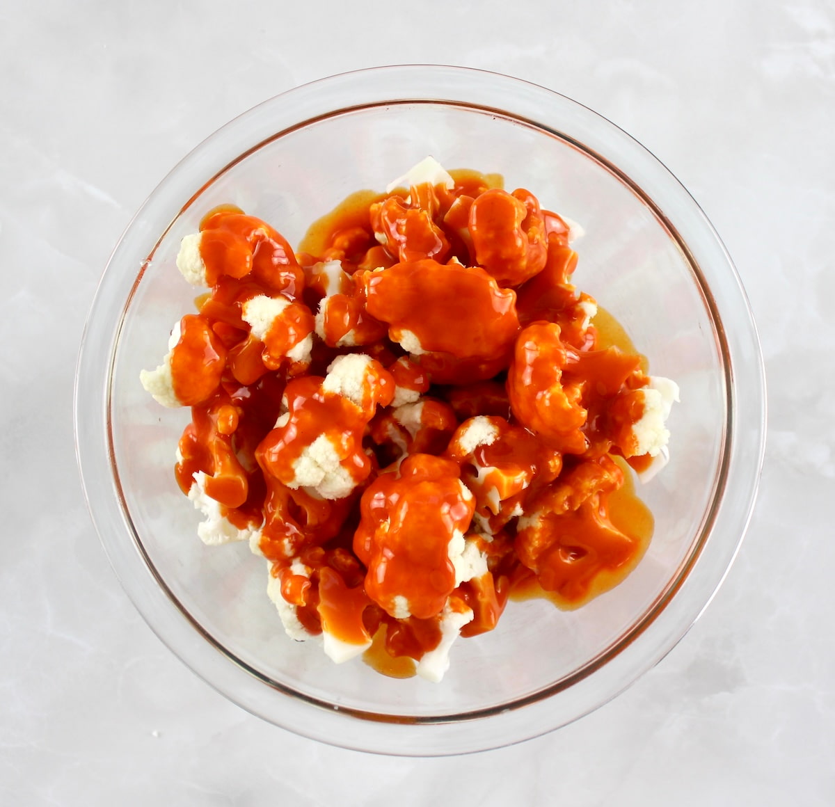 cauliflower florets in glass bowl with buffalo sauce over the top