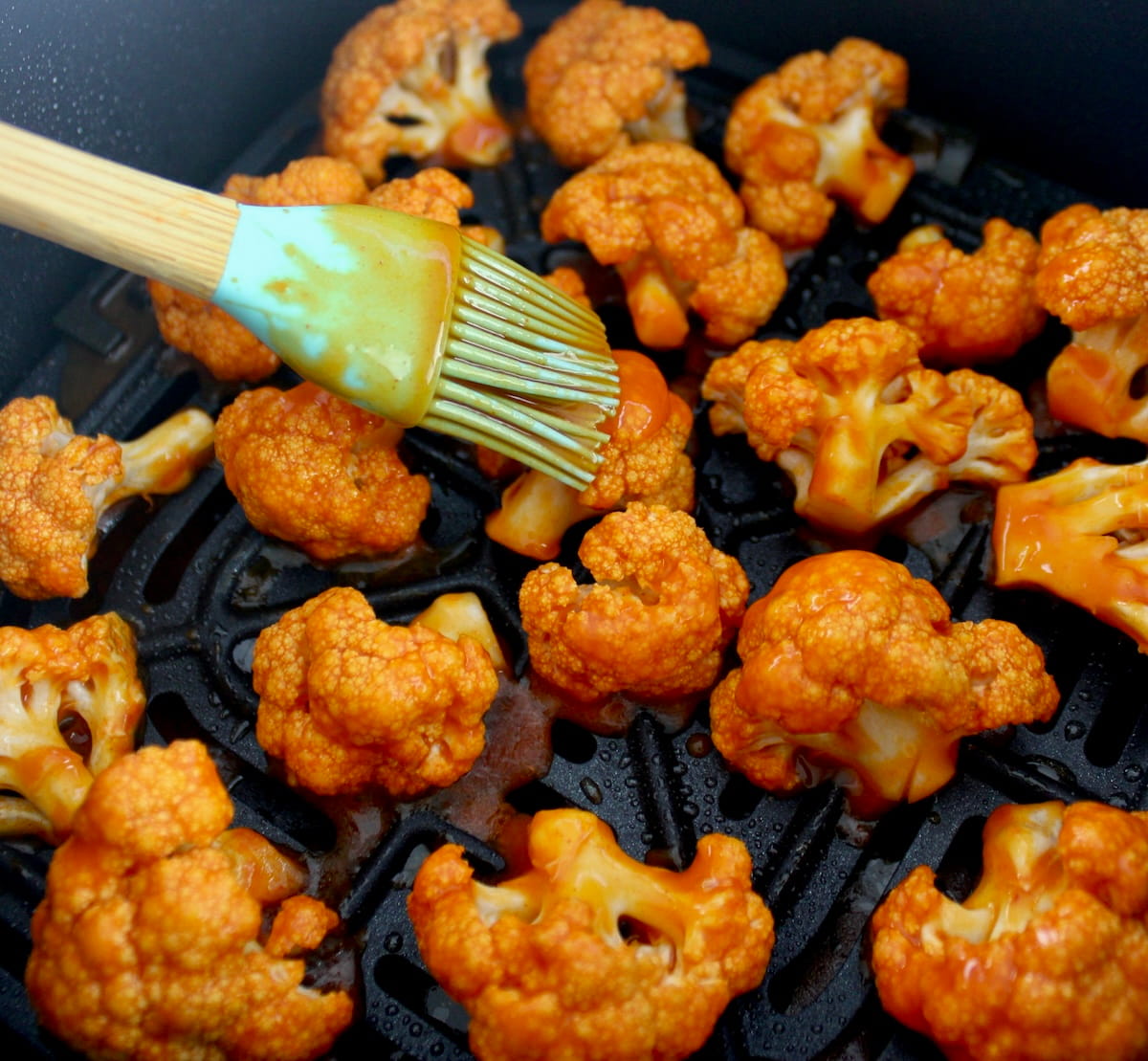 Air Fryer Buffalo Cauliflower in air fryer basket with wing sauce being brushed on top