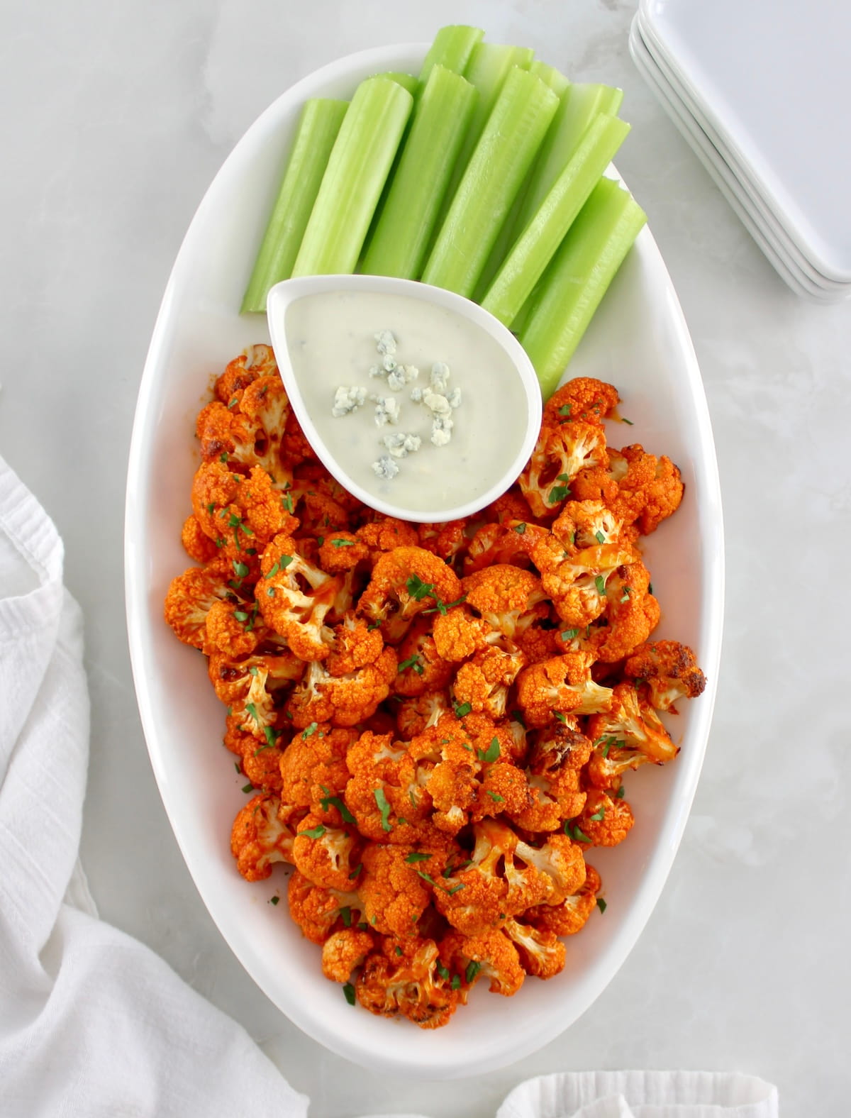 overhead view of Air Fryer Buffalo Cauliflower on white oval plate with blue cheese and celery
