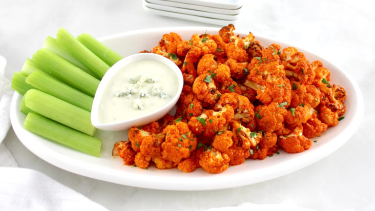 Air Fryer Buffalo Cauliflower on white oval plate with celery and blue cheese on side