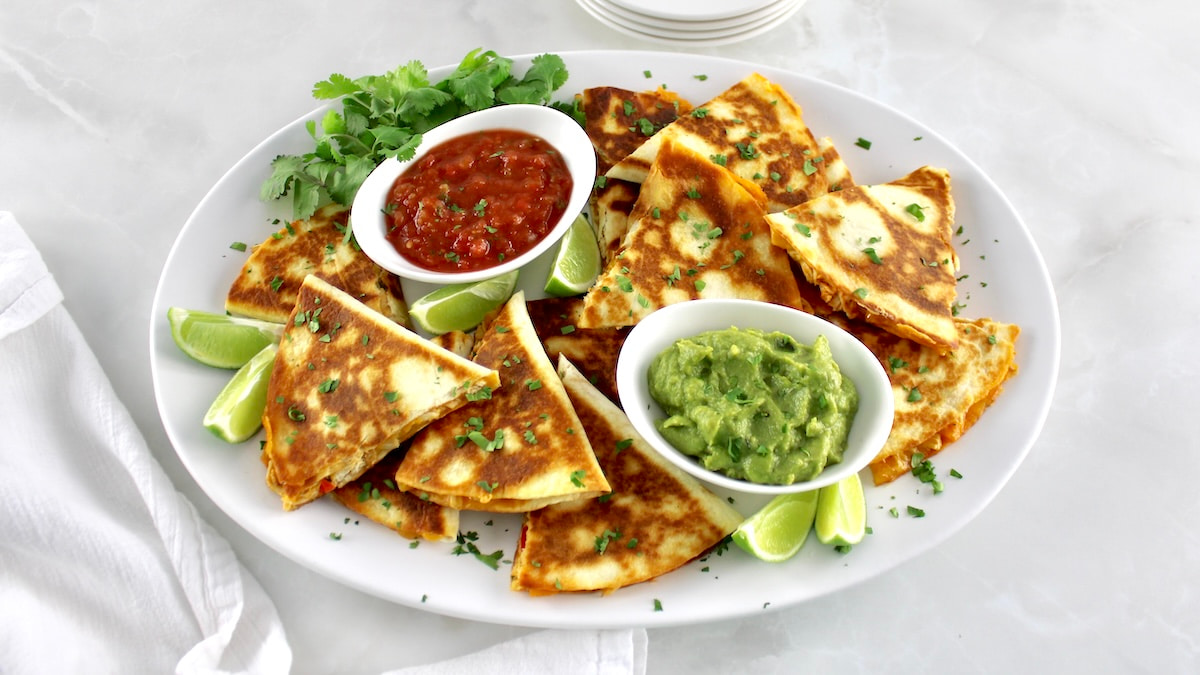 overhead view of Easy Chicken Quesadillas on white oval platter with salsa and guacamole