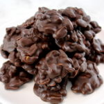 Keto Chocolate Peanut Clusters piled up on white cake stand
