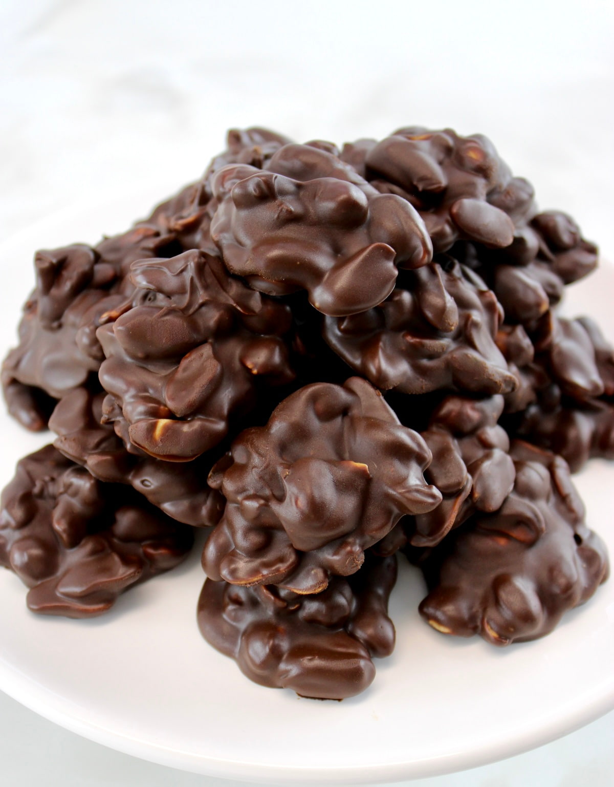 Keto Chocolate Peanut Clusters piled up on white cake stand