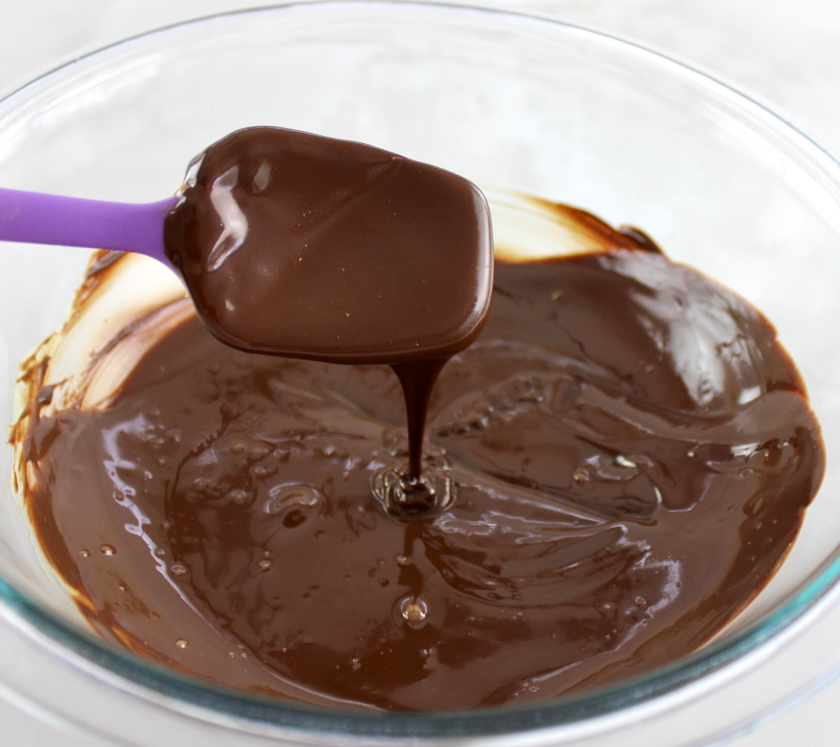 melted chocolate in glass bowl with spoon dripping chocolate