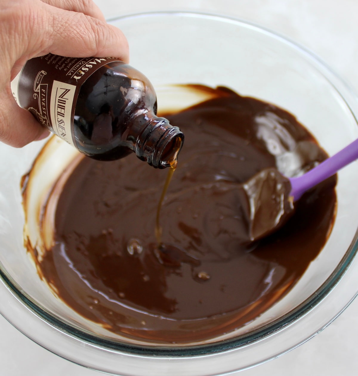 vanilla extract being poured into glass bowl with melted chocolate