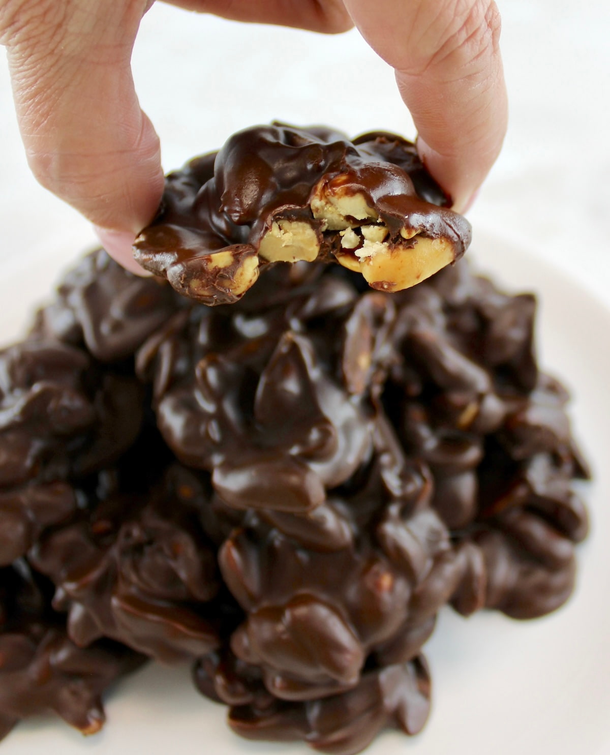 holding up Keto Chocolate Peanut Cluster with bite taken out