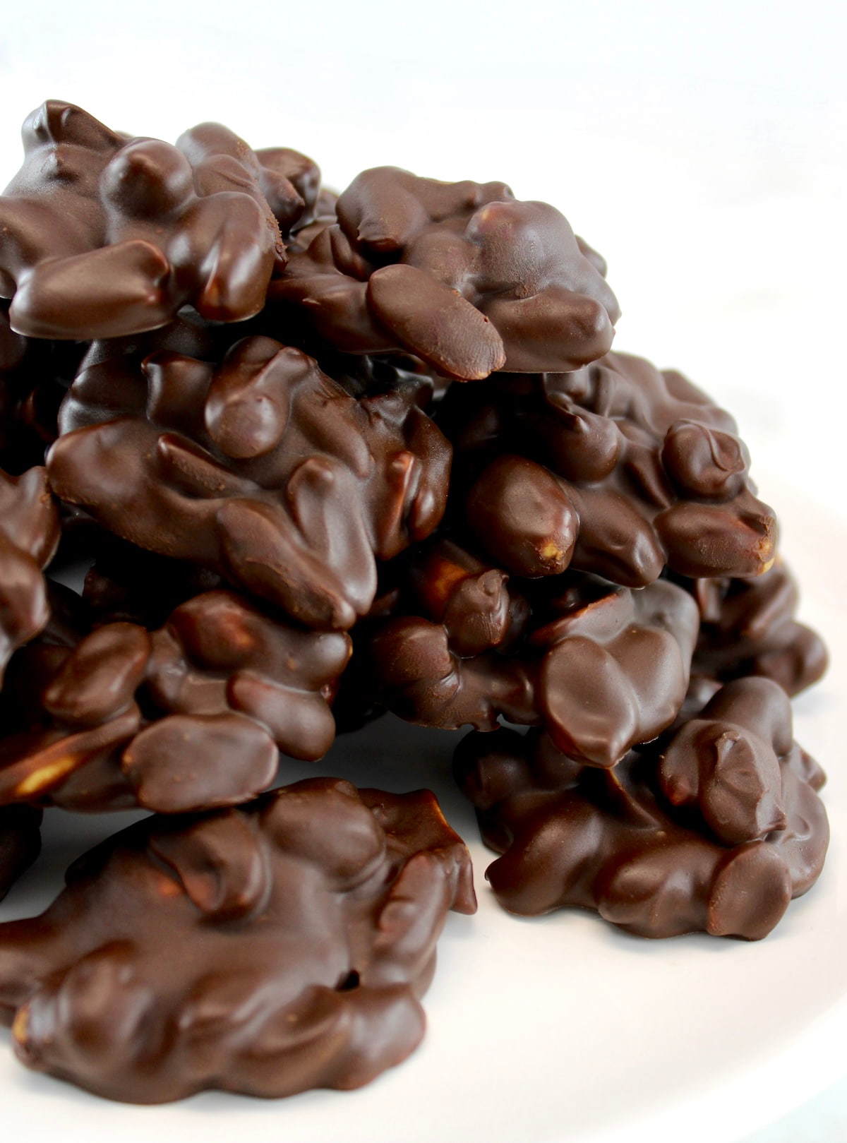 closeup side view of Keto Chocolate Peanut Clusters piled up on white plate