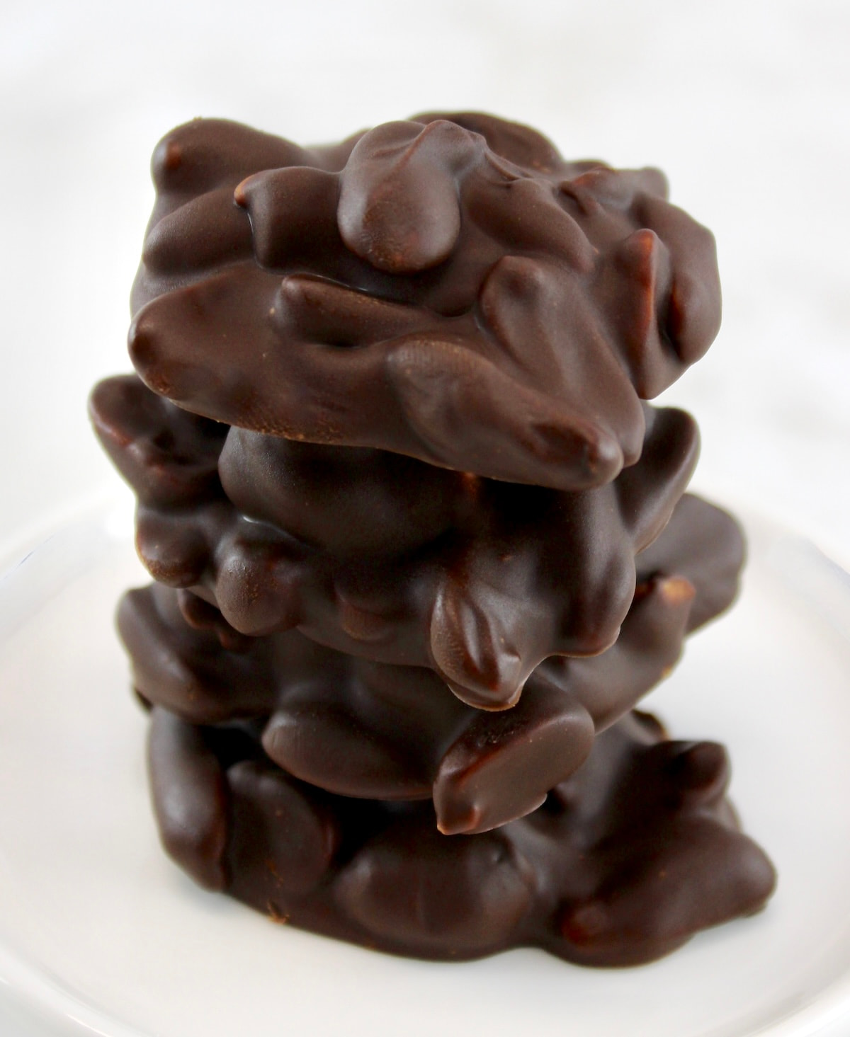 Keto Chocolate Peanut Clusters stacked up on upon another on white plate
