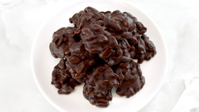 Keto Chocolate Peanut Clusters piled up on white cake stand