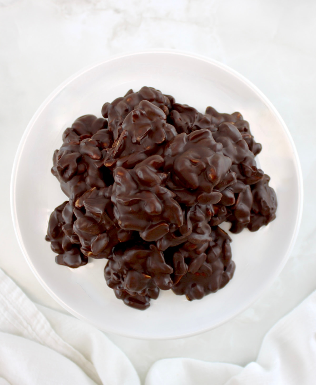 overhead view of Keto Chocolate Peanut Clusters piled up on white plate