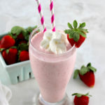 Keto Strawberry Milkshake in glass with 2 pink straws and strawberry on side