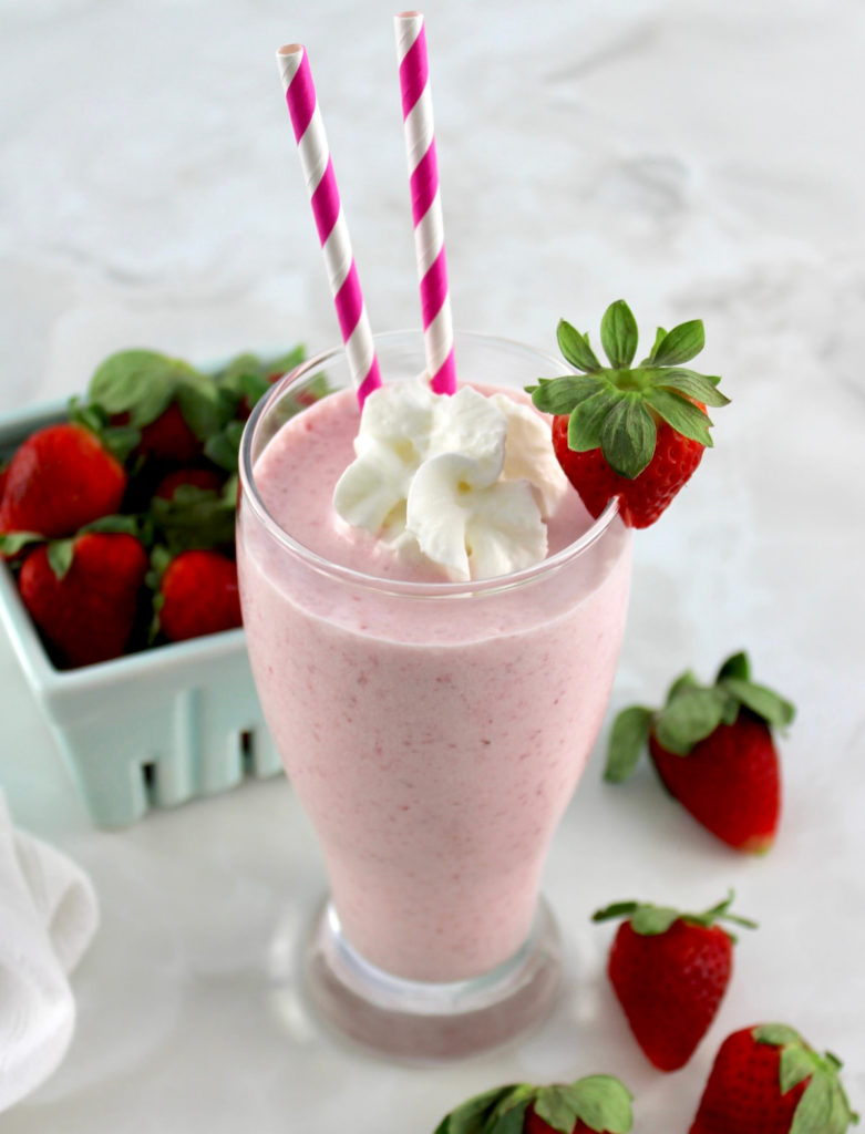 Keto Strawberry Milkshake in glass with 2 pink straws and strawberry on side