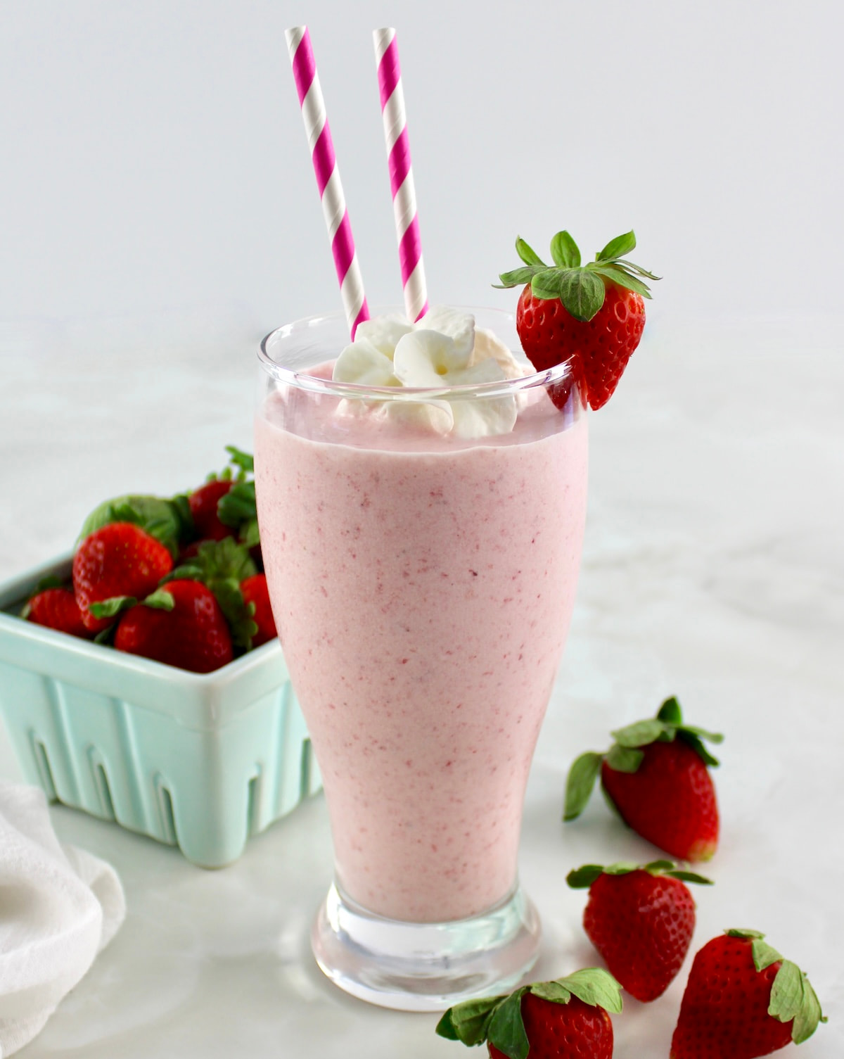 side view of Keto Strawberry Milkshake in glass with strawberry on side and 2 pink straws