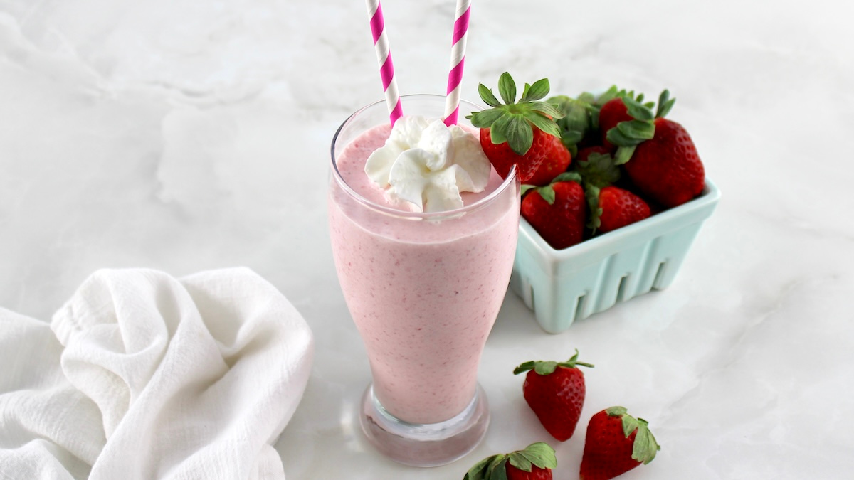 side view of Keto Strawberry Milkshake in glass with 2 straws and strawberry on side