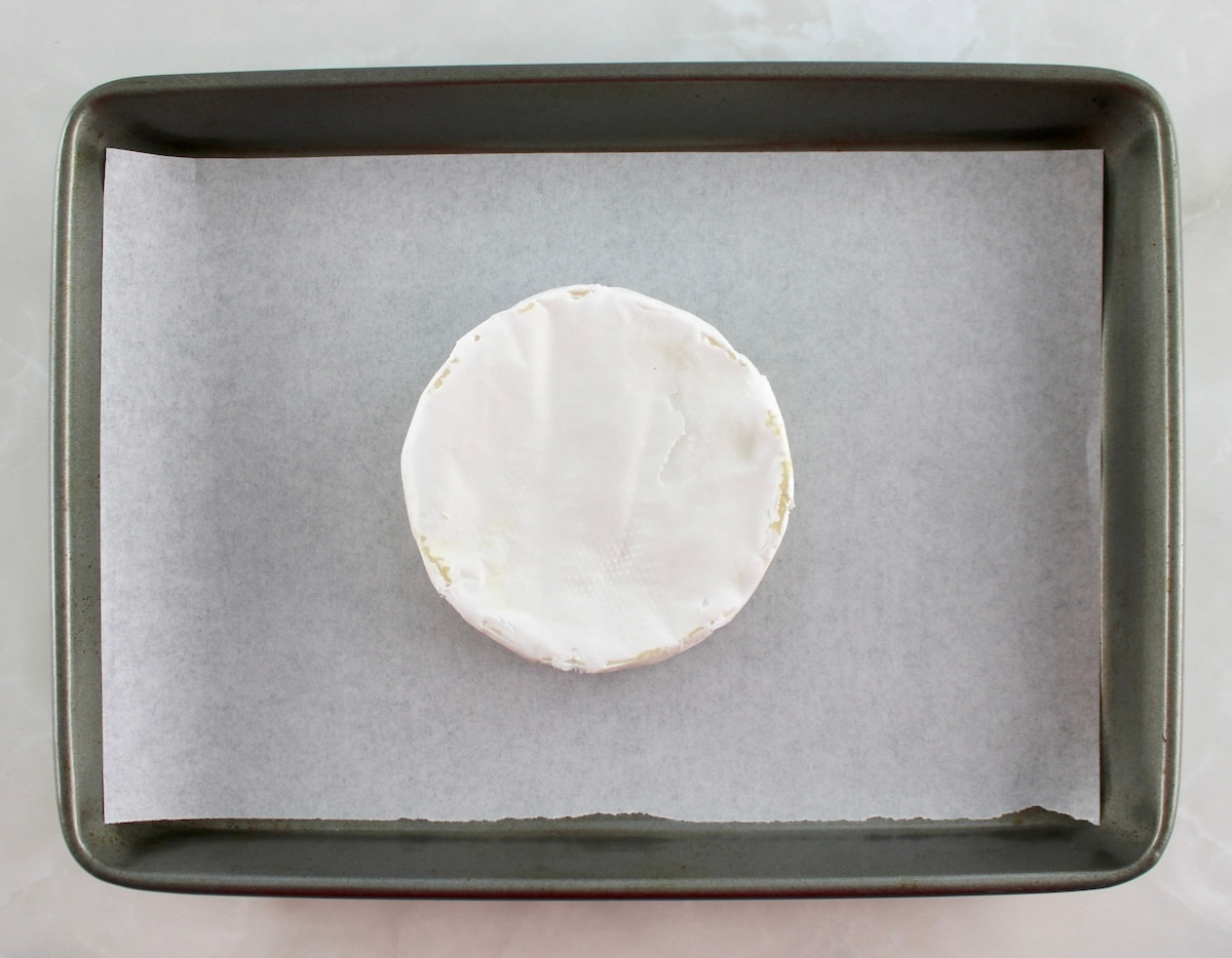 wheel of brie cheese on baking sheet lined with parchment paper