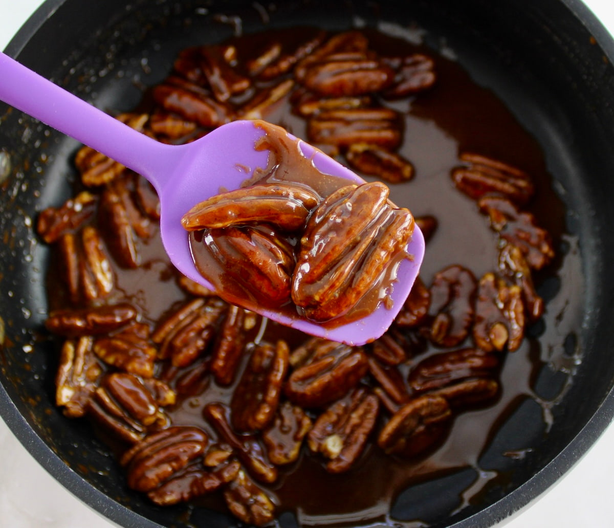 purple spatula holding up pecans in caramel sauce