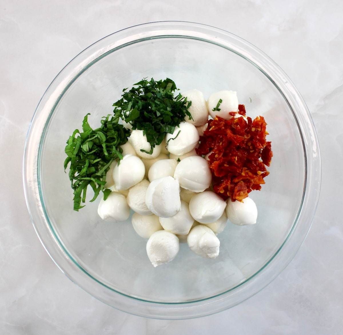 glass bowl with mozzarella balls, sun-dried tomatoes, chopped basil and parsley unmixed