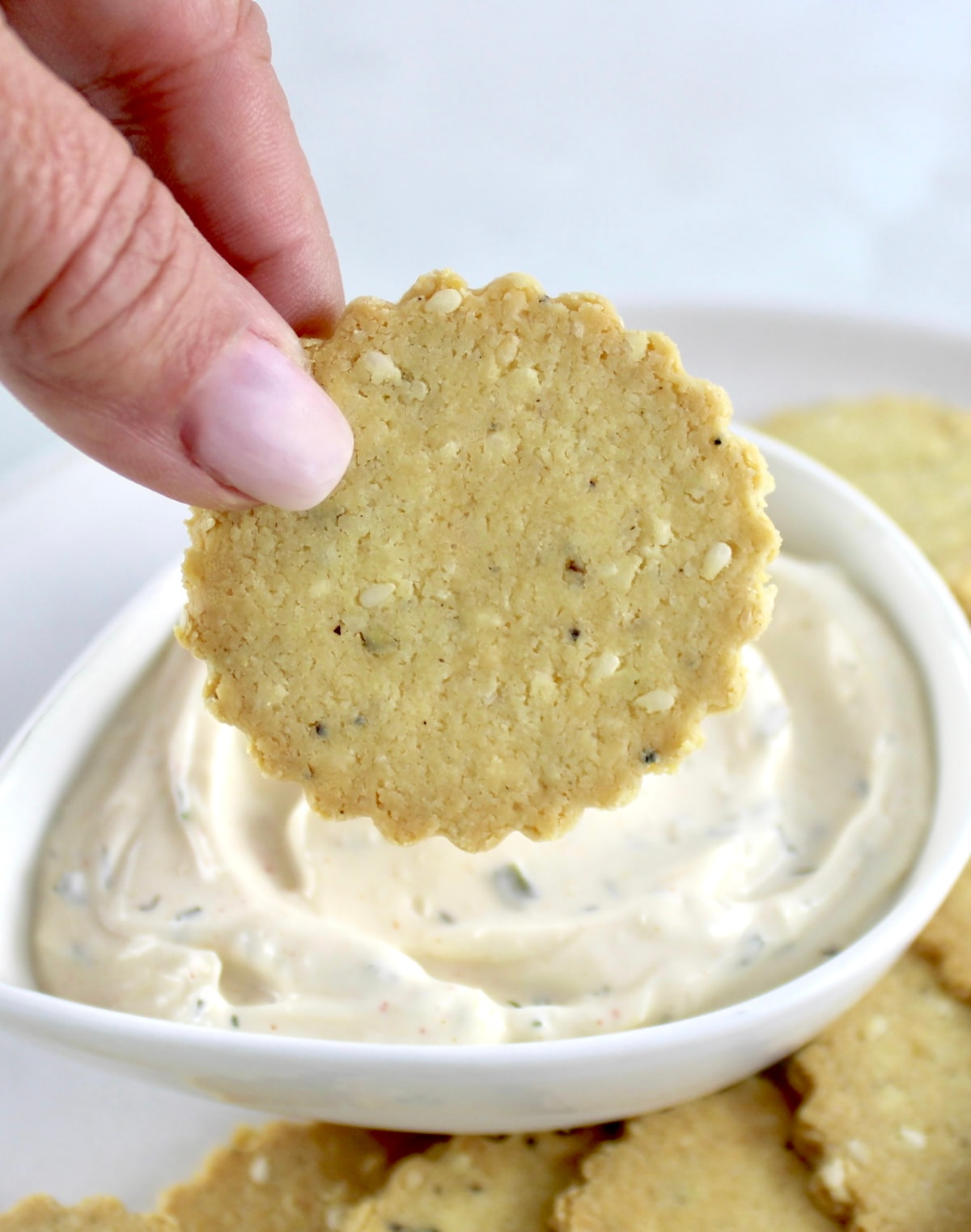 holding up Sesame Almond Flour Cracker over dip in white bowl
