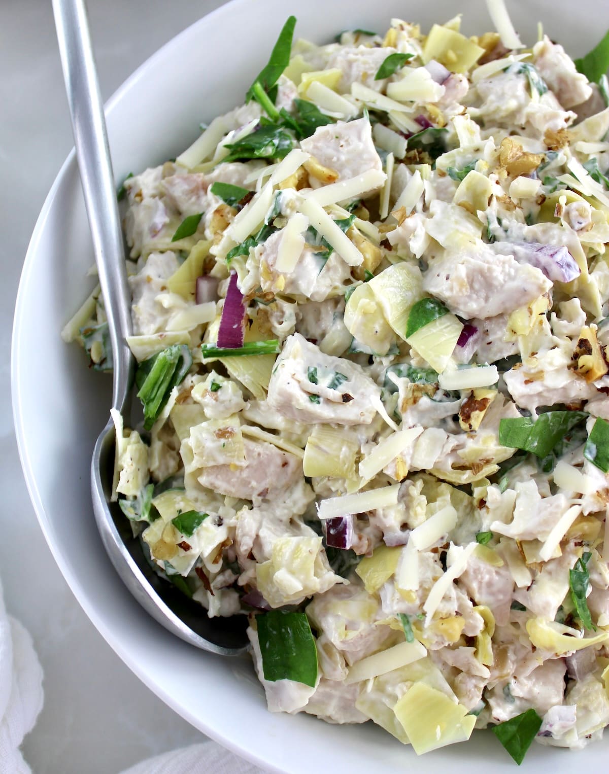 closeup of Spinach Artichoke Chicken Salad in white bowl with spoon on side