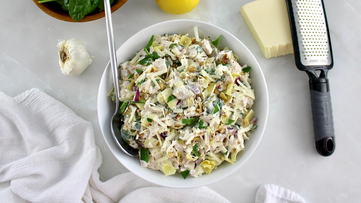 overhead view of Spinach Artichoke Chicken Salad in white bowl with spoon on side