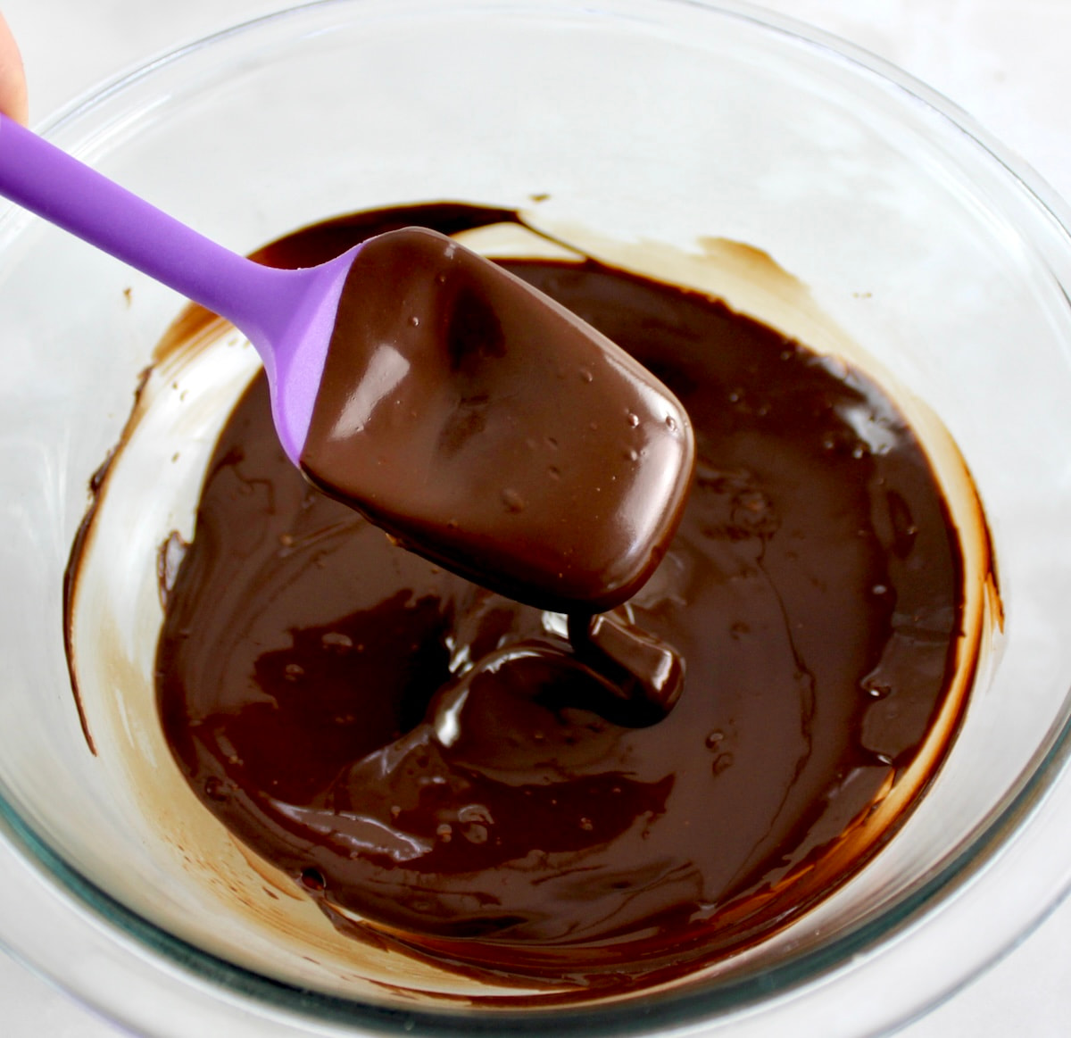 melted chocolate in glass bowl with purple spoon dripping