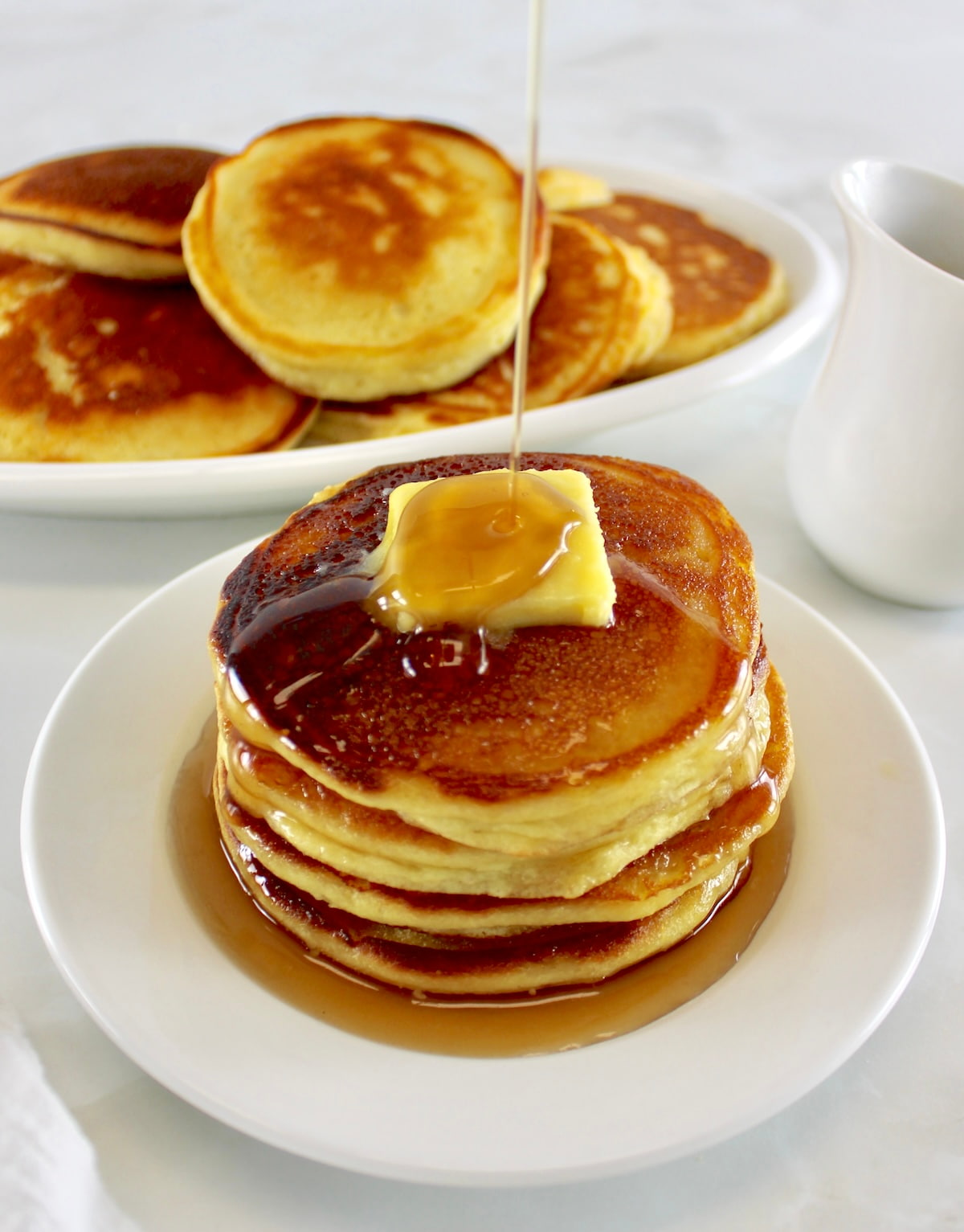stack of Keto Ricotta Pancakes on white dish with pad of butter and syrup pouring on top