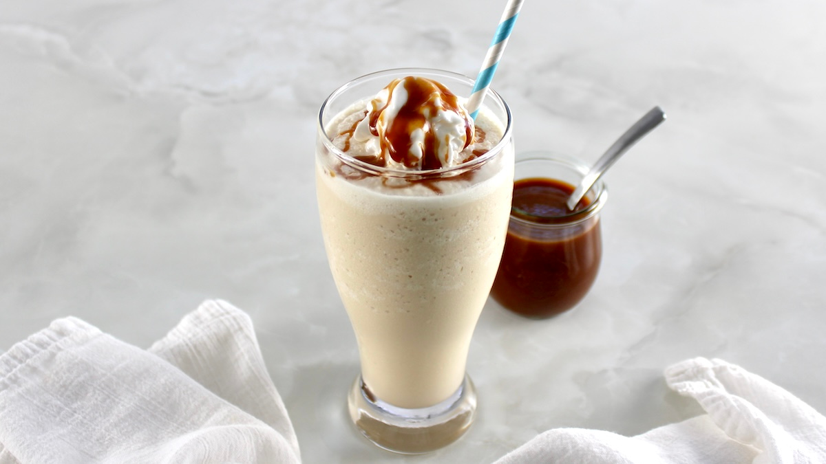 side view of Keto Salted Caramel Milkshake in glass with caramel in back