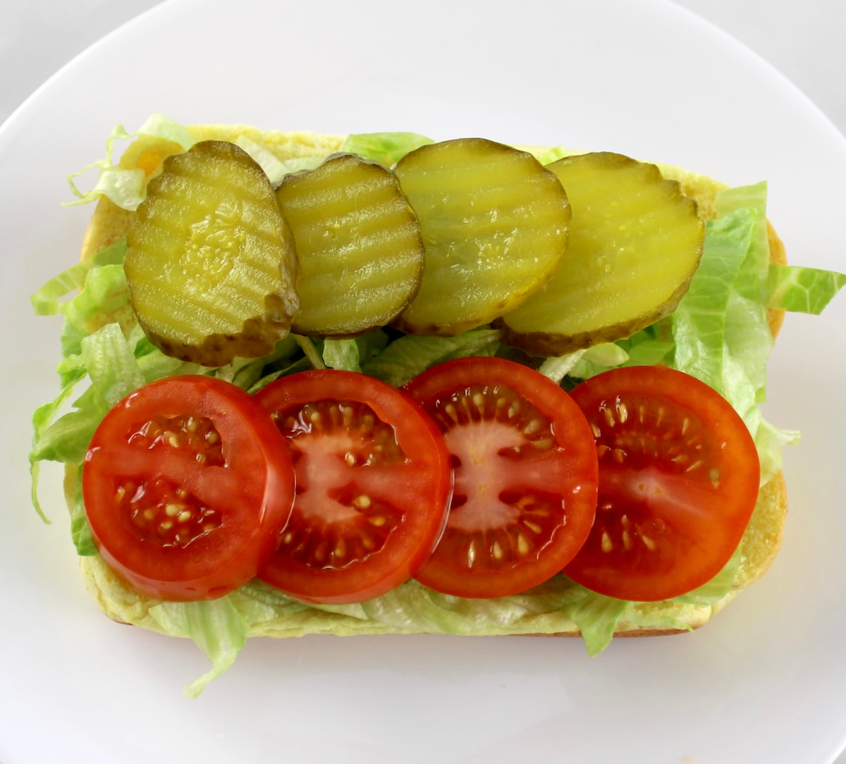 hot dog bun with shredded lettuce, sliced pickles and tomatoes
