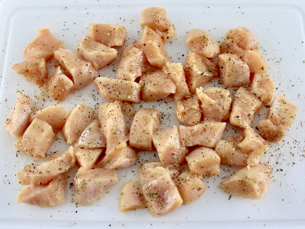 cubes of raw chicken with dried herbs on white cutting board