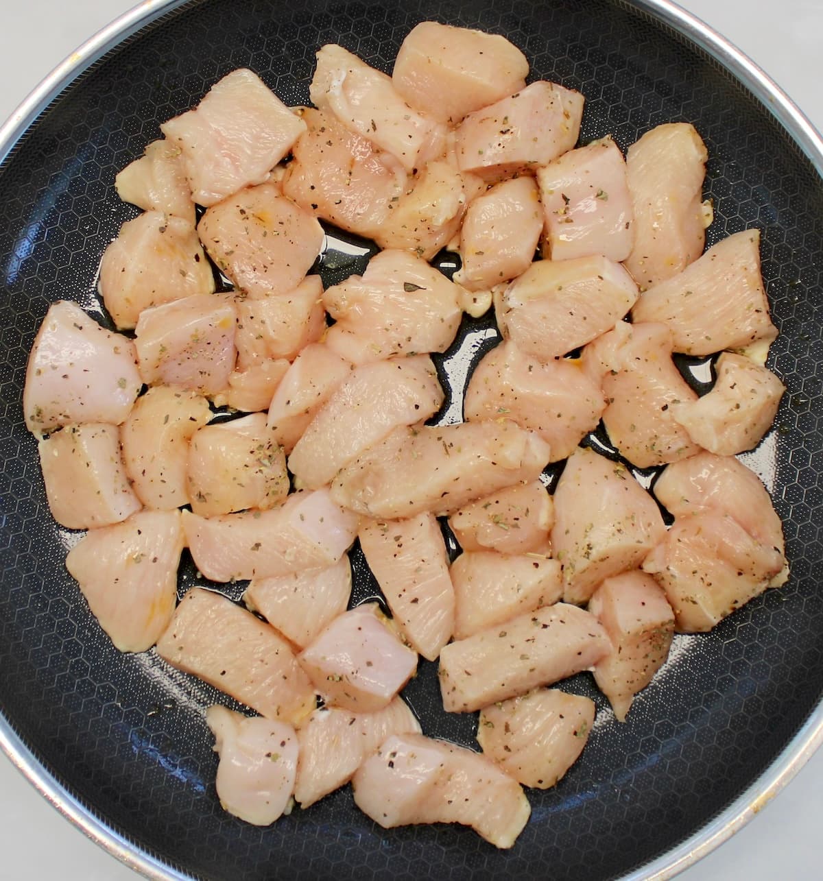cubes of raw chicken with dried herbs in skillet