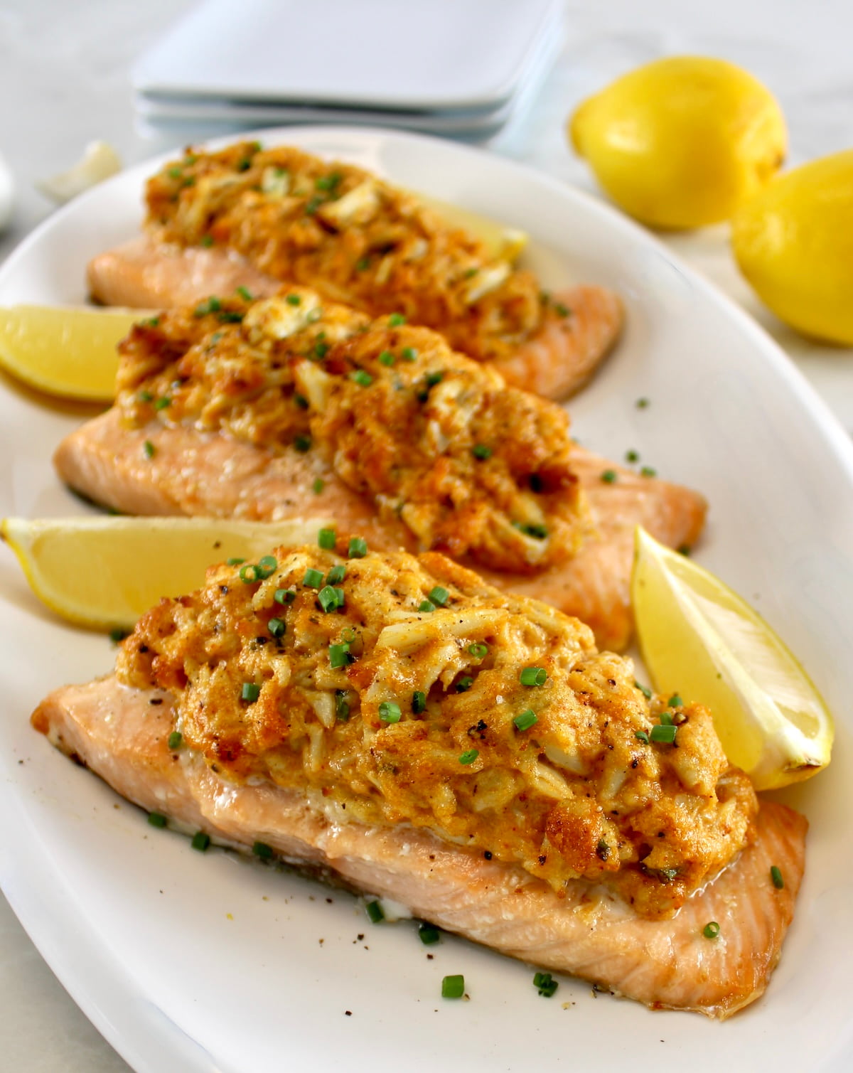 3 pieces of Cajun Crab Stuffed Salmon on white plate with lemon wedges