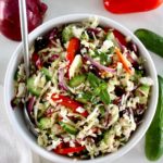 overhead view of Greek Coleslaw in white bowl with silver serving spoon on side